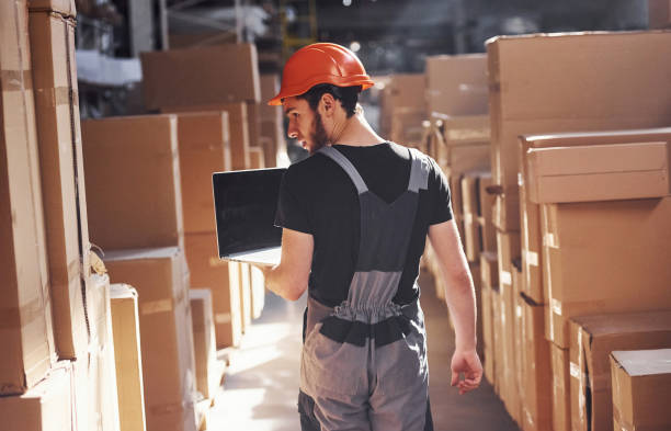istock Storage worker in uniform and modern laptop in hands checks production 1317436021