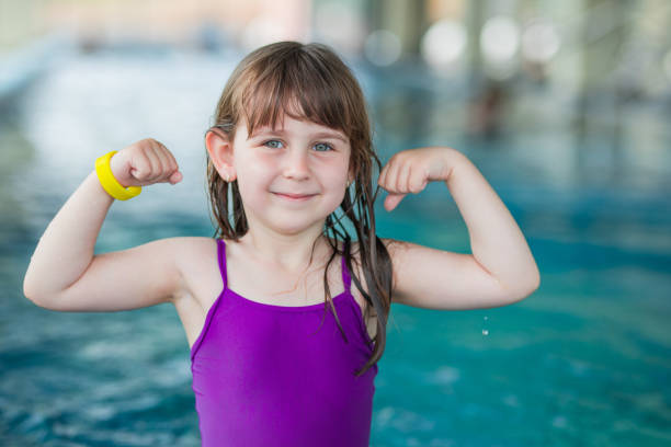 jeune fille heureuse restant dans la piscine et fléchissant ses muscles - little girls flexing muscles swimming swimwear photos et images de collection