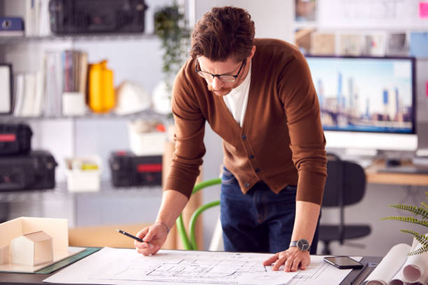 istock Male Architect Standing At Desk In Office Amending Building Plans 1317442703