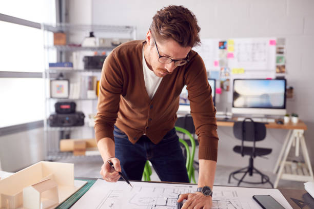 istock Male Architect Standing At Desk In Office Amending Building Plans 1317442836