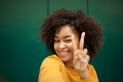 Portrait of smiling african american young woman taking selfie with peace hand sign