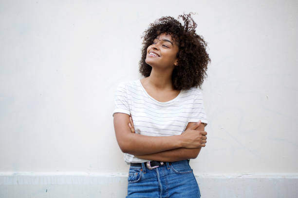 gelukkige jonge afrikaanse amerikaanse vrouw die met gekruiste wapens glimlacht en weg tegen witte achtergrond kijkt - volwassen vrouwen stockfoto's en -beelden