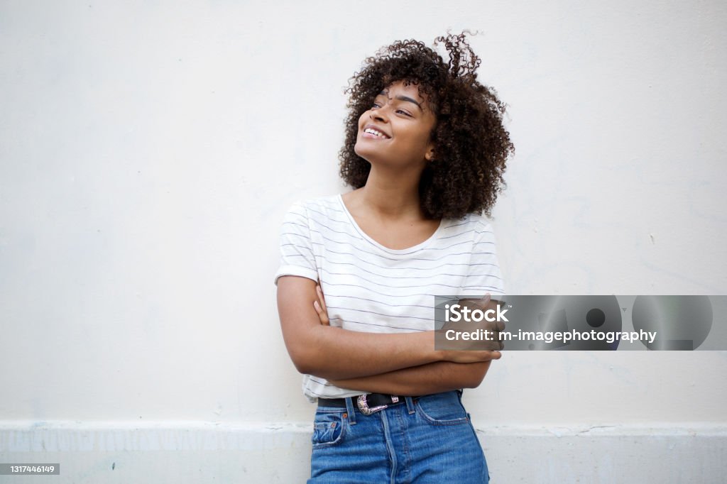 happy young african american woman smiling with arms crossed and looking away against white background Portrait of happy young african american woman smiling with arms crossed and looking away against white background Women Stock Photo