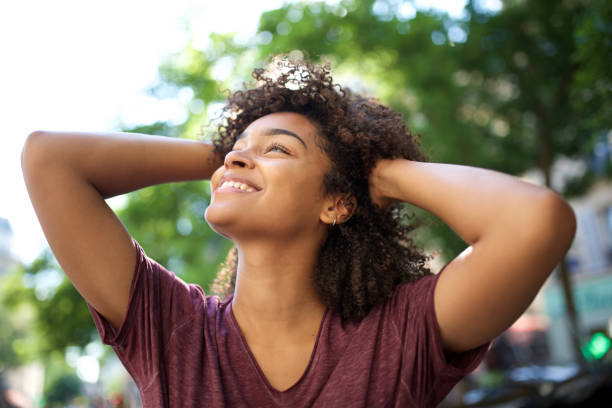 niña afroamericana sonriente con las manos en el pelo rizado mirando hacia otro lado - mano en el cabello fotografías e imágenes de stock