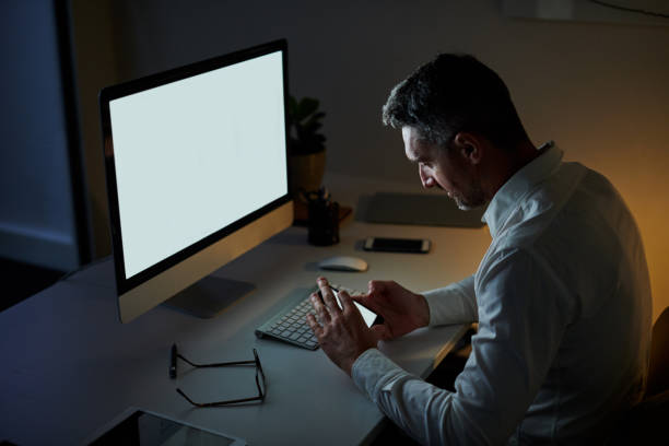 istock Shot of a mature businessman using a cellphone while working on a computer in an office at night 1317449484