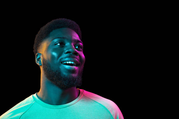 afrikanische junge mann porträt auf dunklen studio hintergrund in neon. konzept der menschlichen emotionen, mimik, jugend, verkauf, anzeige. - neon fotos stock-fotos und bilder