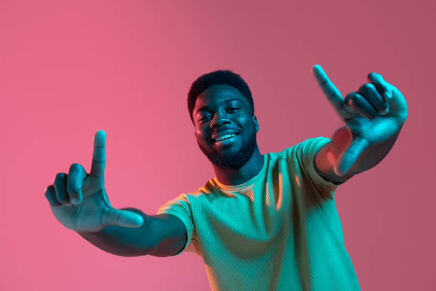 afrikanische junge mann porträt auf rosa studio hintergrund in neon. konzept der menschlichen emotionen, mimik, jugend, verkauf, anzeige. - neon fotos stock-fotos und bilder