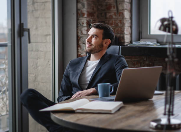 istock Handsome young brunette man businessman in a jacket sits in an office at a table with a laptop and papers 1317456292
