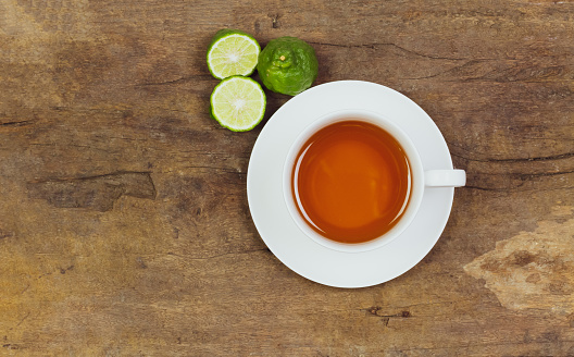 Bergamot tea or Earl Grey tea in white cup and fresh bergamot fruit with sliced on brown wooden table, top view.