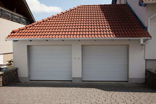 A modern and luxurious two-car garage with a tiled red roof and a roller door. Exterior minimalism.