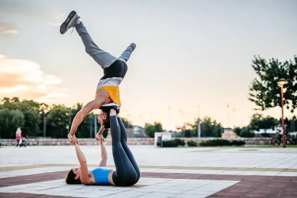 Young Caucasian athlete couple practicing acroyoga in public park.