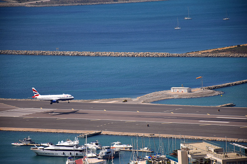 Gibraltar - 16th June, 2022: British Airways aircraft taxis on the Gibraltar airstrip that protrudes into the sea as a boat passes by. Gibraltar is a British Overseas Territory