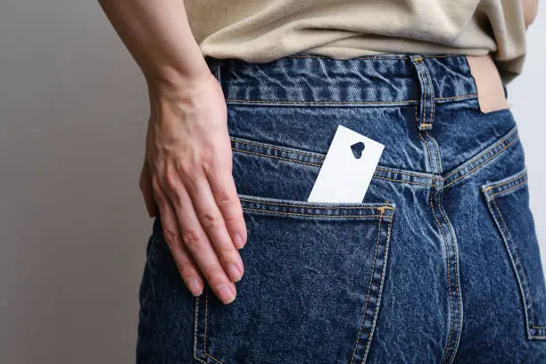 Photo of White card with a cut out heart in a girl's jeans pocket. Close-up postcard. Flat lay. Form for congratulations on Valentine's Day. A romantic invitation. Mockup. Cute message or invitation on paper.