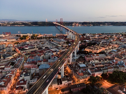 Aerial view of April 25th bridge with Christ the King statue (Cristo Rei) in background at sunset, view of Lisbon skyline at night, Alcântara, Lisbon, Portugal.