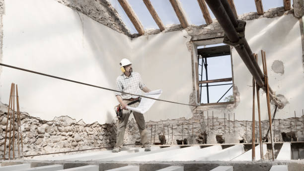 istock man at work, construction worker wearing helmet and looking at blueprint , check the house project plan, in renovation building site background with the beams at the base of the foundations 1317476112