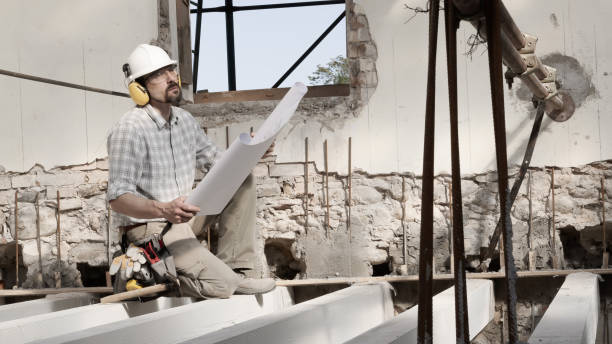 istock man at work, construction worker wearing helmet and looking at blueprint , check the house project plan, in renovation building site background with the beams at the base of the foundations 1317476185