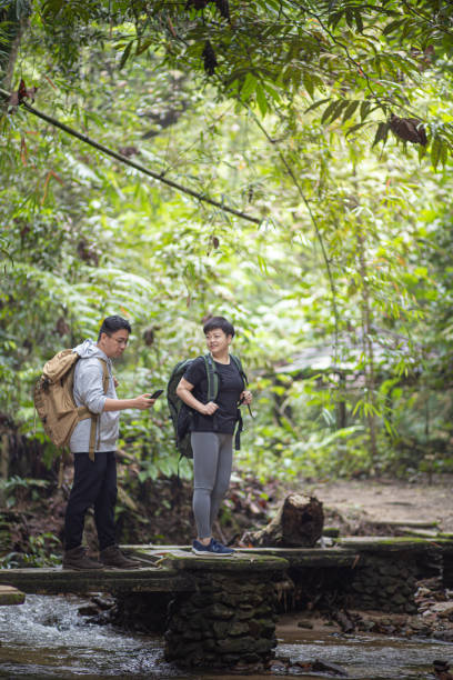 istock Asian Chinese couple using mobile app on map for direction navigation hiking and exploring forest 1317476453