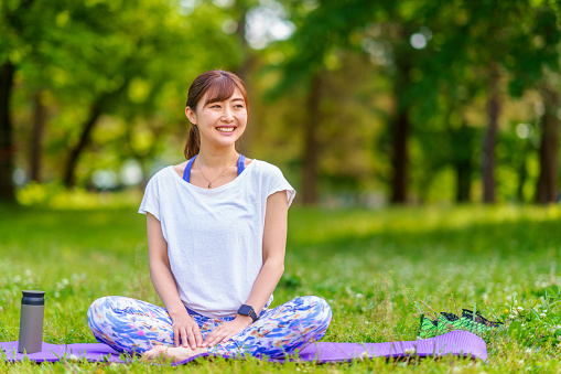A portrait of a sports woman sitting on an exercise mat and smiling for the camera in a public park.