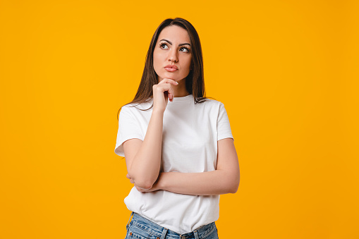 Thoughtful young caucasian woman thinking about shopping, love, relationship, gossip isolated on yellow background. Pensive young latin-american woman dreaming about new house, making plans for future