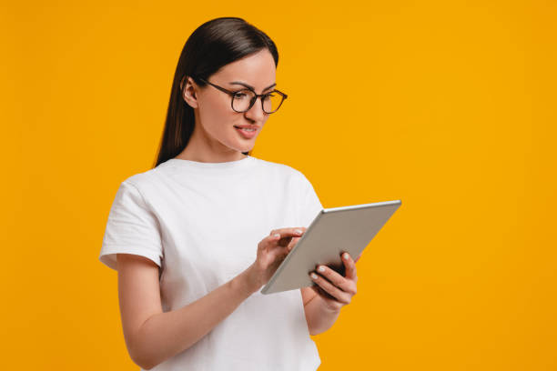 Smart intelligent caucasian hispanic latin-american young woman student using digital tablet isolated over yellow background. Clever young female office worker chatting on tablet, sending messages, watching online webinars
