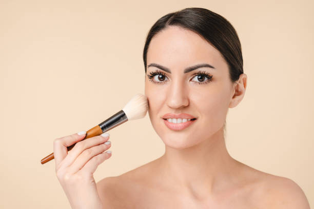 istock Charming caucasian young woman female applying makeup with brush using blusher on her cheeks with bare shoulders. Beauty, cosmetology concept 1317480024