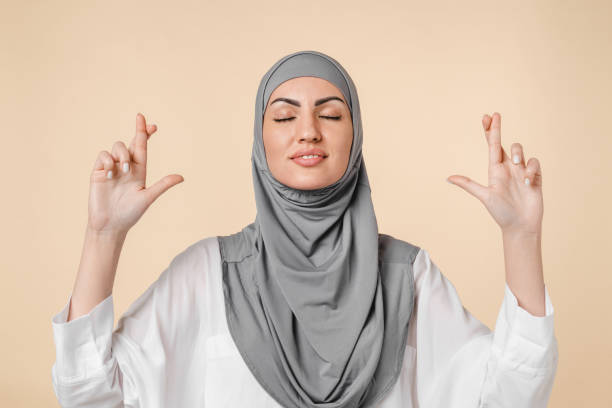 희망 개념, 젊은 아라비아 중동 이슬람 이슬람 예쁜 여자 회색 히잡을 통해 행운을 위해 손가락을 교차, 희망 베이지 색 배경에 고립 된 기적을 기대. 미신 제스처 - pleading women business sadness 뉴스 사진 이미지