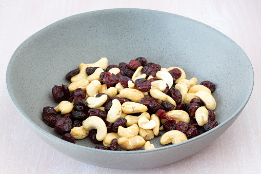 close-up of cashew nuts and dried cranberries in a bowl on white background
