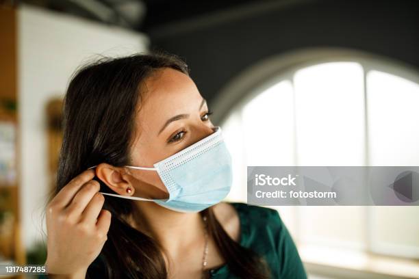 Young Woman Putting On A Protective Face Mask Stock Photo - Download Image Now - Protective Face Mask, Getting Dressed, Indoors