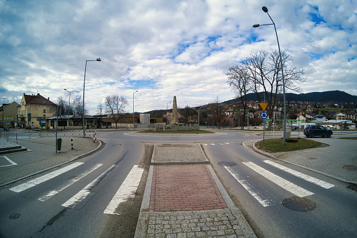 Limanowa, Poland - April 01, 2021: Main city Center cross road shows zebra cross against monument made of stone with beautify mountains in the background.