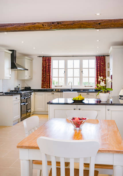 Farmhouse kitchen UK Farmhouse kitchen furniture design. UK open plan farmhouse kitchen interior with modern painted wood kitchen units, wooden breakfast table and chairs white units stock pictures, royalty-free photos & images