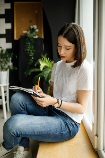 istock Young university student sitting on a window sill and writing in her notebook 1317492053