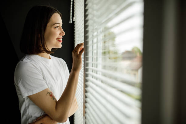 istock Smiling young woman looking through the window and smiling 1317492400