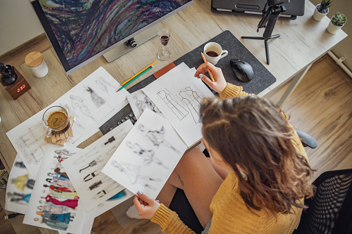 A young woman sits in her workspace in the apartment, uses a computer and designs new projects.