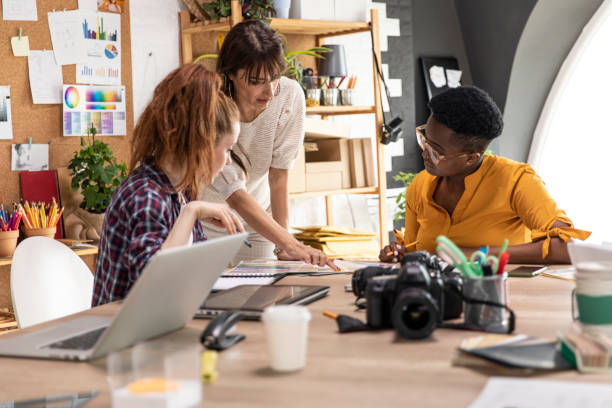 Three female colleagues having a business meeting at the graphic design studio Candid shot of three creative female entrepreneurs collaborating on a project together, discussing ideas and strategies together at the graphic design studio. design studio stock pictures, royalty-free photos & images