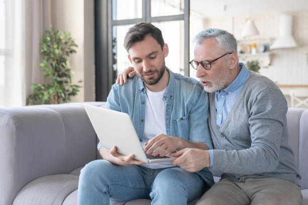 istock Helpful young adult son helping aiding his old senior elderly father in using laptop for watching movies, communicating online. Son teaching father how to use laptop. Happy father`s day! 1317496472