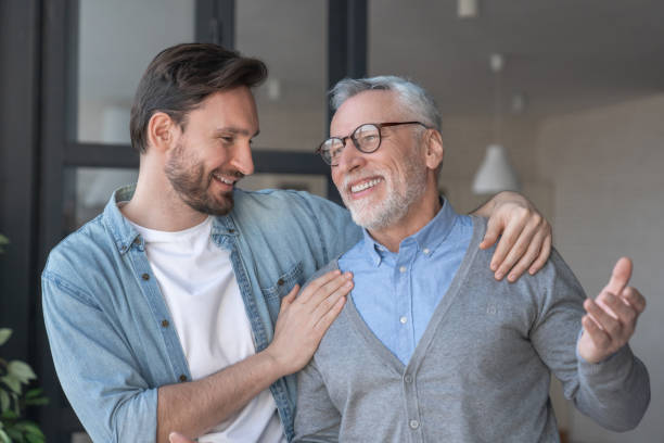 Young adult caucasian son listening and supporting his old elderly senior father at home indoors.Happy father`s day! Care and love concept. I love you, dad! stock photo