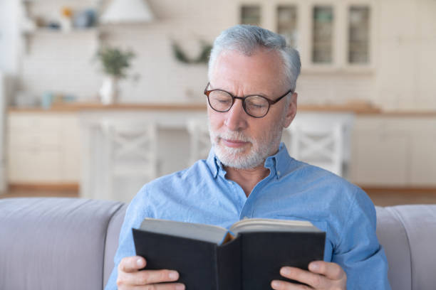 istock Caucasian mature senior old elderly man with grey hair reading book at home, e-learning indoors, active seniors. Grandfather`s leisure activity 1317496878
