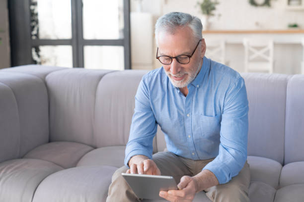 istock Cheerful old elderly grandfather, senior man using digital tablet, searching web, using social media, loading feed, doing online shopping at home sitting on the sofa 1317497155