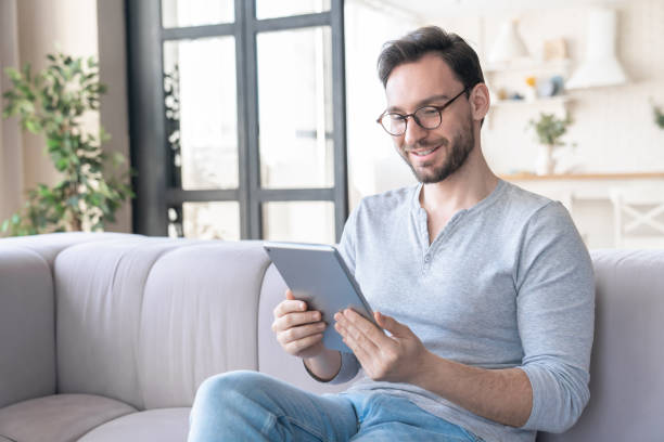 istock Confident young caucasian man using digital tablet sitting on the sofa, relaxing and reading e-book, e-learning, checking social media, doing online shopping at home indoors 1317497878