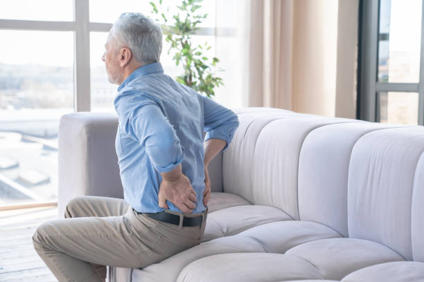 senior kaukasischen alten älteren mann leidet unter rückenschmerzen zu hause. rheuma, schmerzen, gesundheitliche probleme. sitzender lebensstil. menschen-, gesundheits- und problemkonzept - human spine chiropractic adjustment backache human bone stock-fotos und bilder