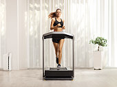 Young woman in shorts and top running on a treadmill at home