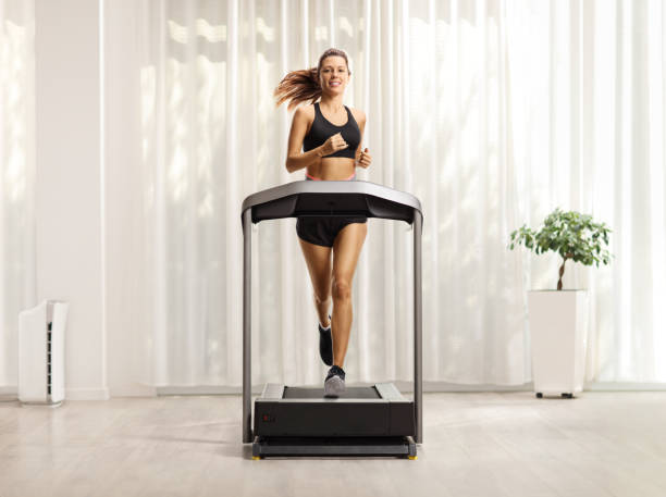 Young woman in shorts and top running on a treadmill at home Full length portrait of a young woman in shorts and top running on a treadmill at home treadmill photos stock pictures, royalty-free photos & images