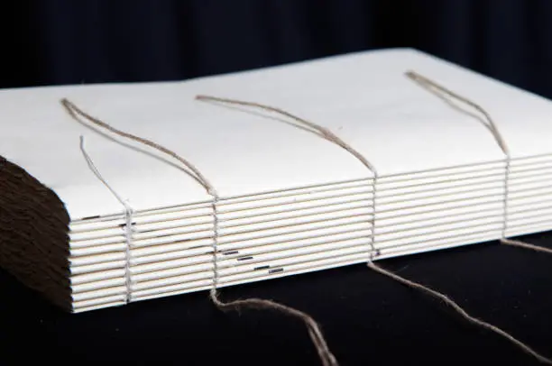 The process of book binding; sewing on cords. Black background