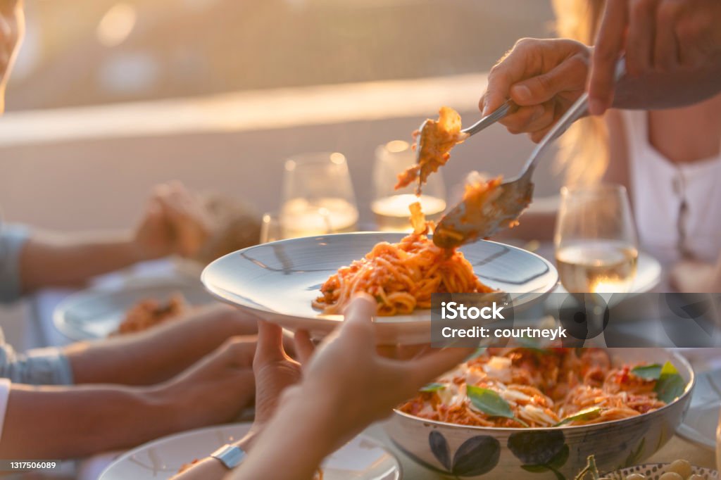 Friends Serving spaghetti Bolognese on a table at sunset. There are glasses of wine and salad on the table; close up tight crop Pasta Stock Photo