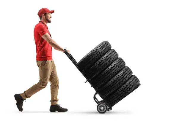 Full length profile shot of a worker pushing a hand truck with tires isolated on white background