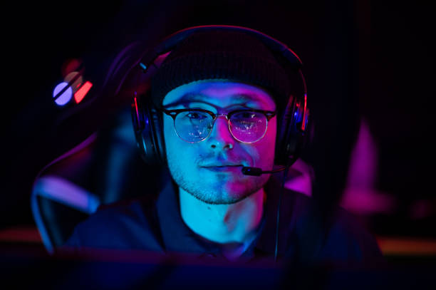 ein junger cybersportler mit brille und headset bei einem esports-turnier. nahaufnahme mit neonlicht - multiplayer stock-fotos und bilder