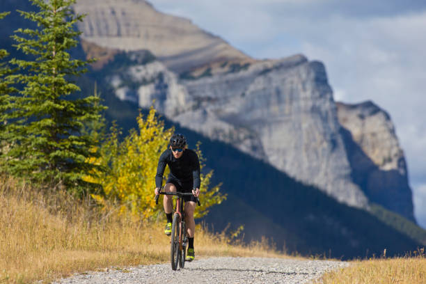 Gravel Road Bicycle Ride A man goes for a gravel road bicycle ride at the Canmore Nordic Centre in Alberta, Canada. Gravel bicycles are similar to cyclocross bikes with strong wheels and tires for riding on rough terrain. He is wearing a bicycle helmet, sunglasses, and road cycling clothing. cycling vest photos stock pictures, royalty-free photos & images