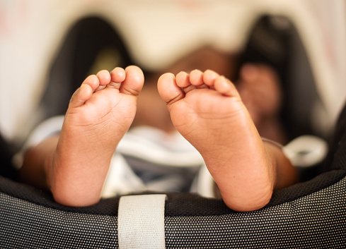 Close-up of a cute little African baby's girls bare feet while lying in an infant safety seat/carrier