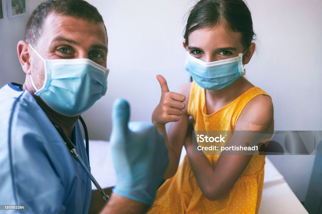 Happy little girl with adhesive bandage on her hand taking a picture with a doctor after vaccination Happy little girl with adhesive bandage on her hand taking a picture with a doctor after COVID-19 vaccine. Child Stock Photo