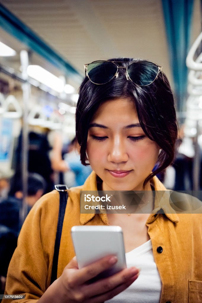 Woman with smart phone traveling in subway train Beautiful woman using cellphone. Young female is using smart phone in subway train. She is wearing casual. 20-24 Years Stock Photo